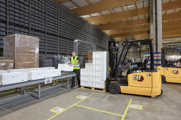 Cat Electric Forklift driver unloading crates onto conveyor belt