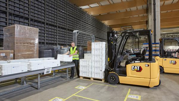 Cat Electric Forklift driver unloading crates onto conveyor belt